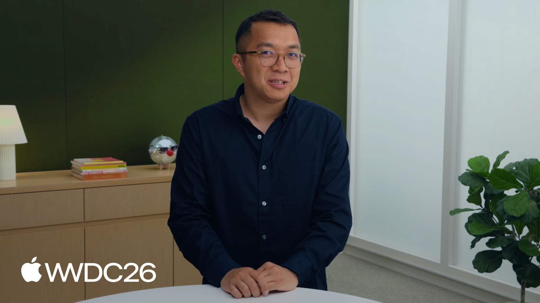 Image of the presenter Tim Nguyen in a dark blue shirt in a room with a plant on the right and a green wall behind him