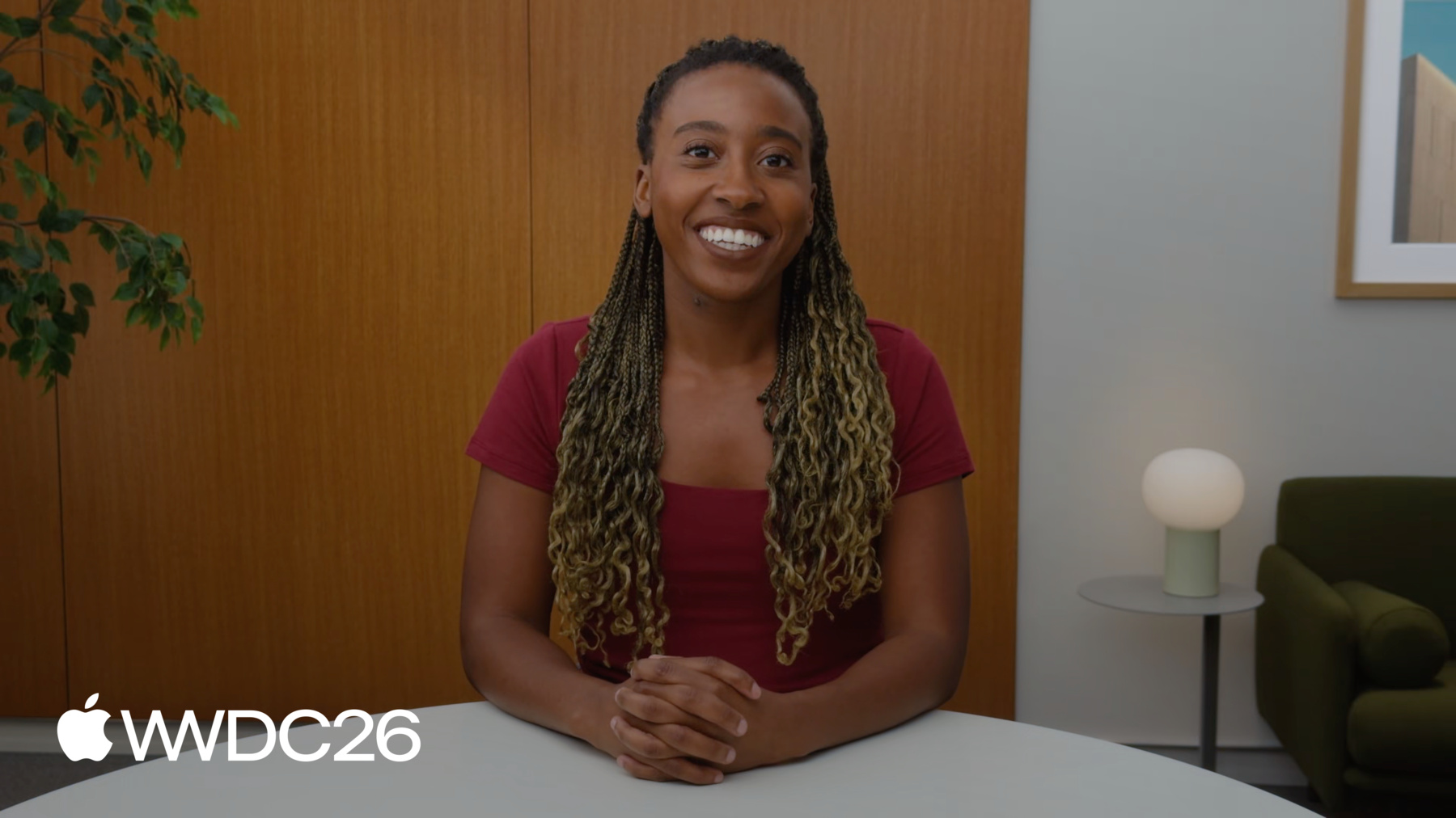 An image of the presenter, Kiara Rose wearing a red top in a room with a wood panel wall and a small side table with a modern-style lamp