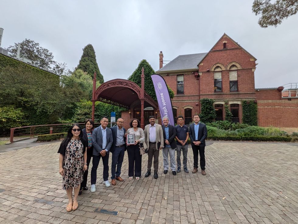 Group standing with award outside historic brick building and garden walkway