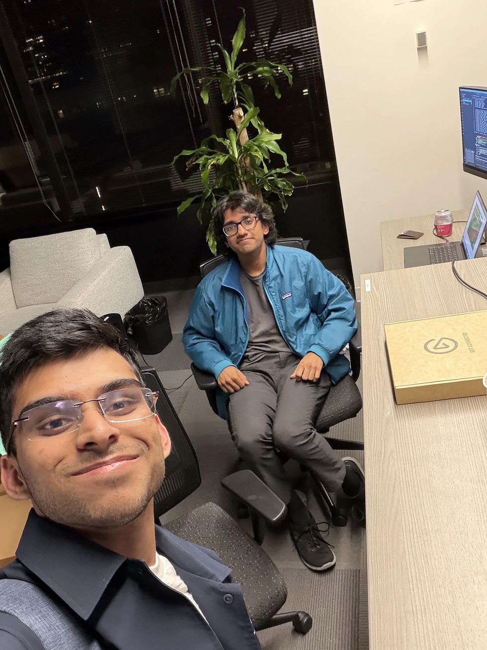 Selfie of two young adult Indian men smiling together in an office environment.