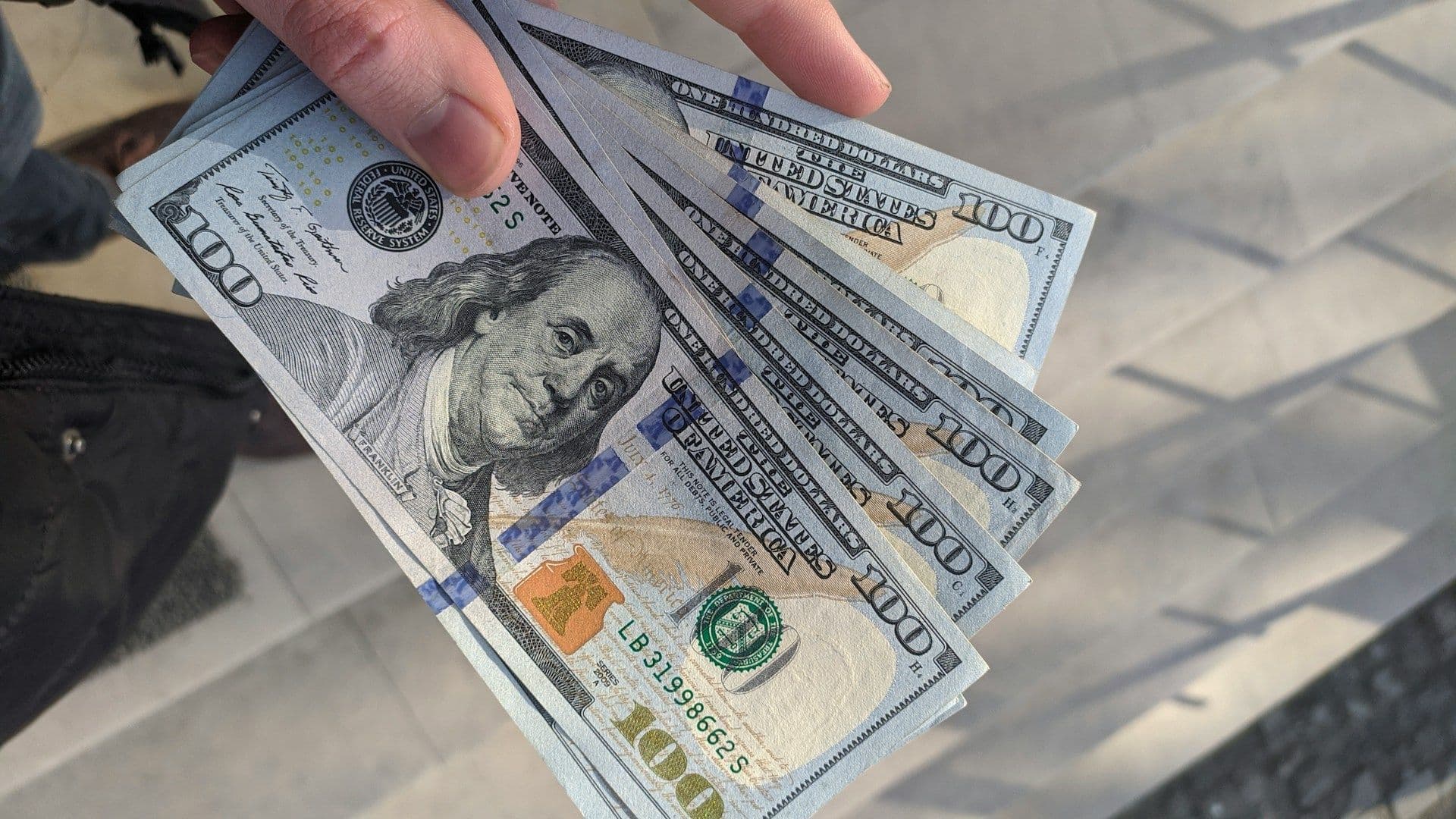 A hand holding several hundred-dollar bills. ( Frederick Warren/Unsplash/Modified by CoinDesk)