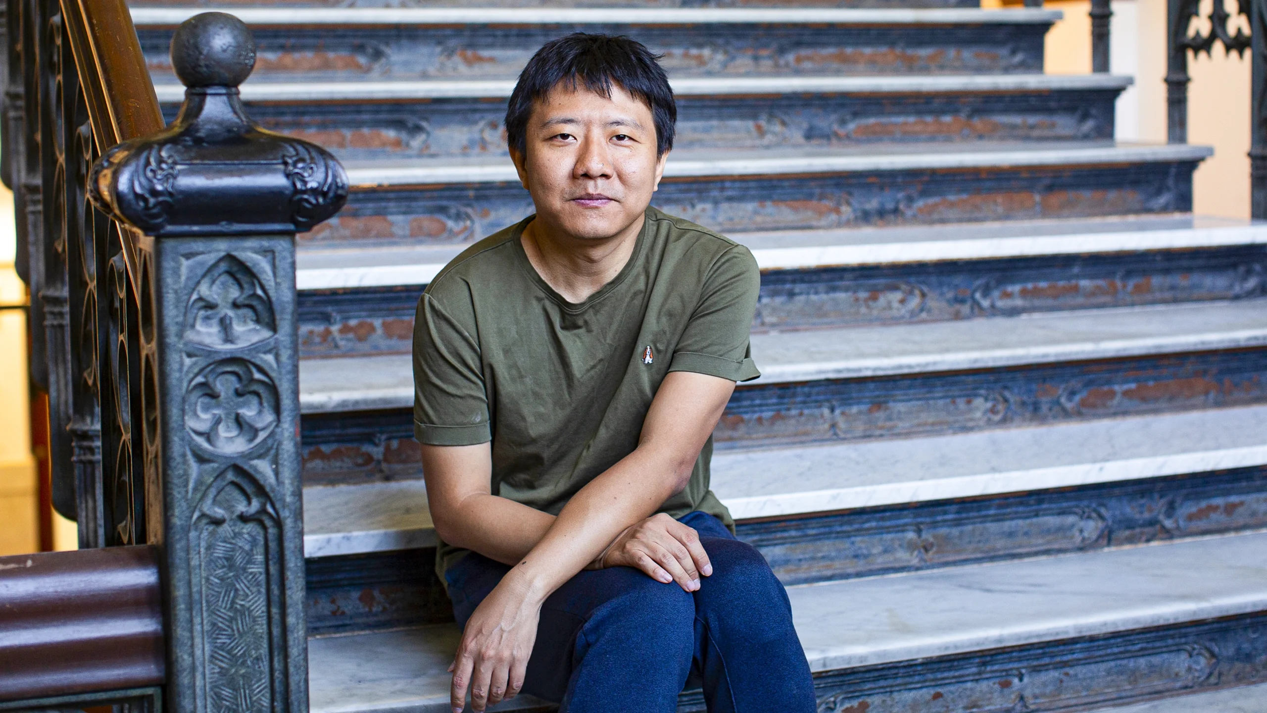 A man in a green shirt sitting on the stairs.