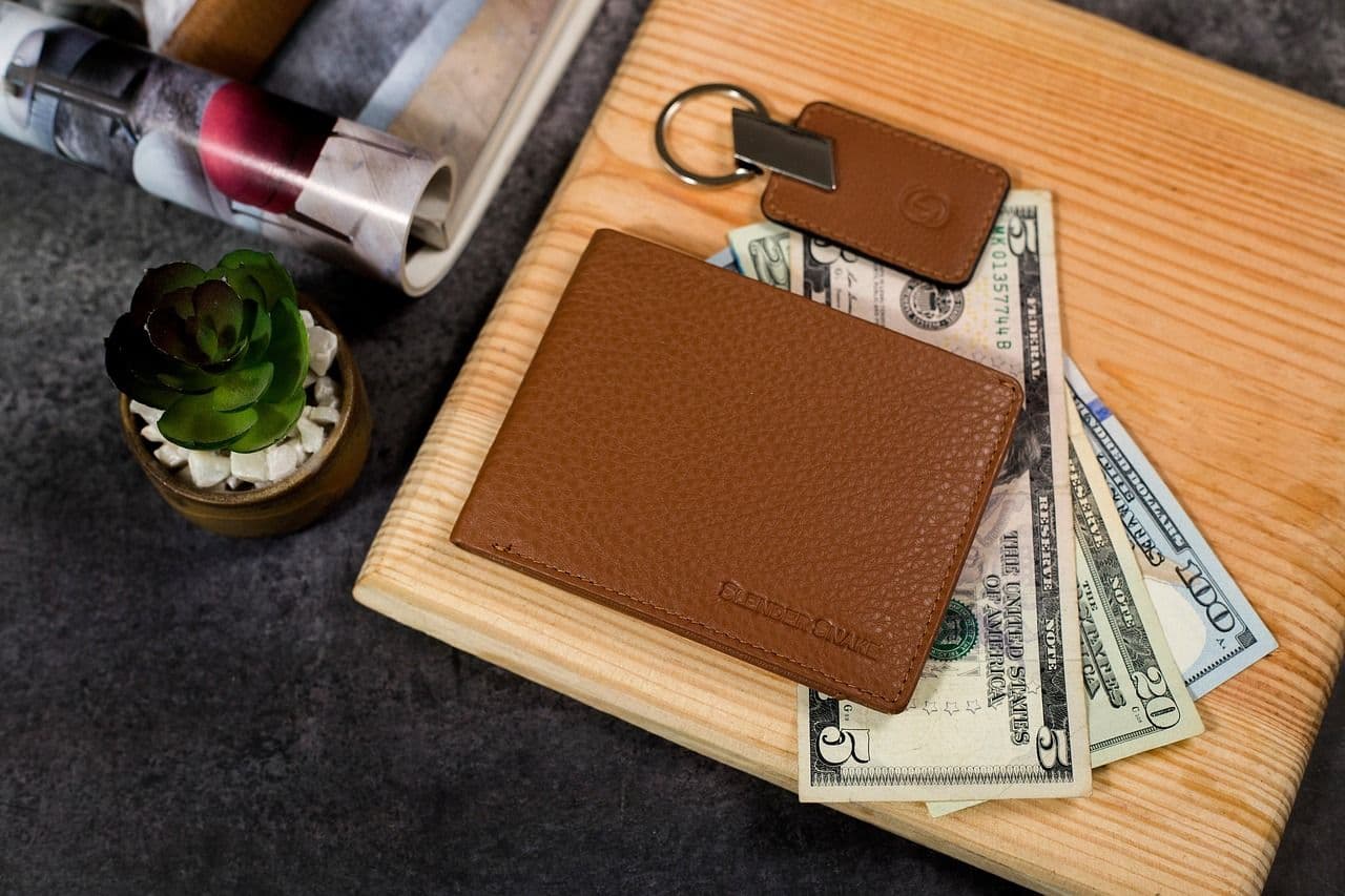 A wallet lies on top of a number of dollar bills. (slendersnakewallet/Pixabay)