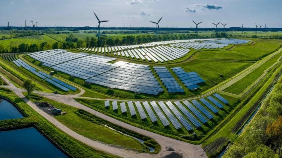 Large solar farm in green fields with wind turbines on the horizon under blue sky