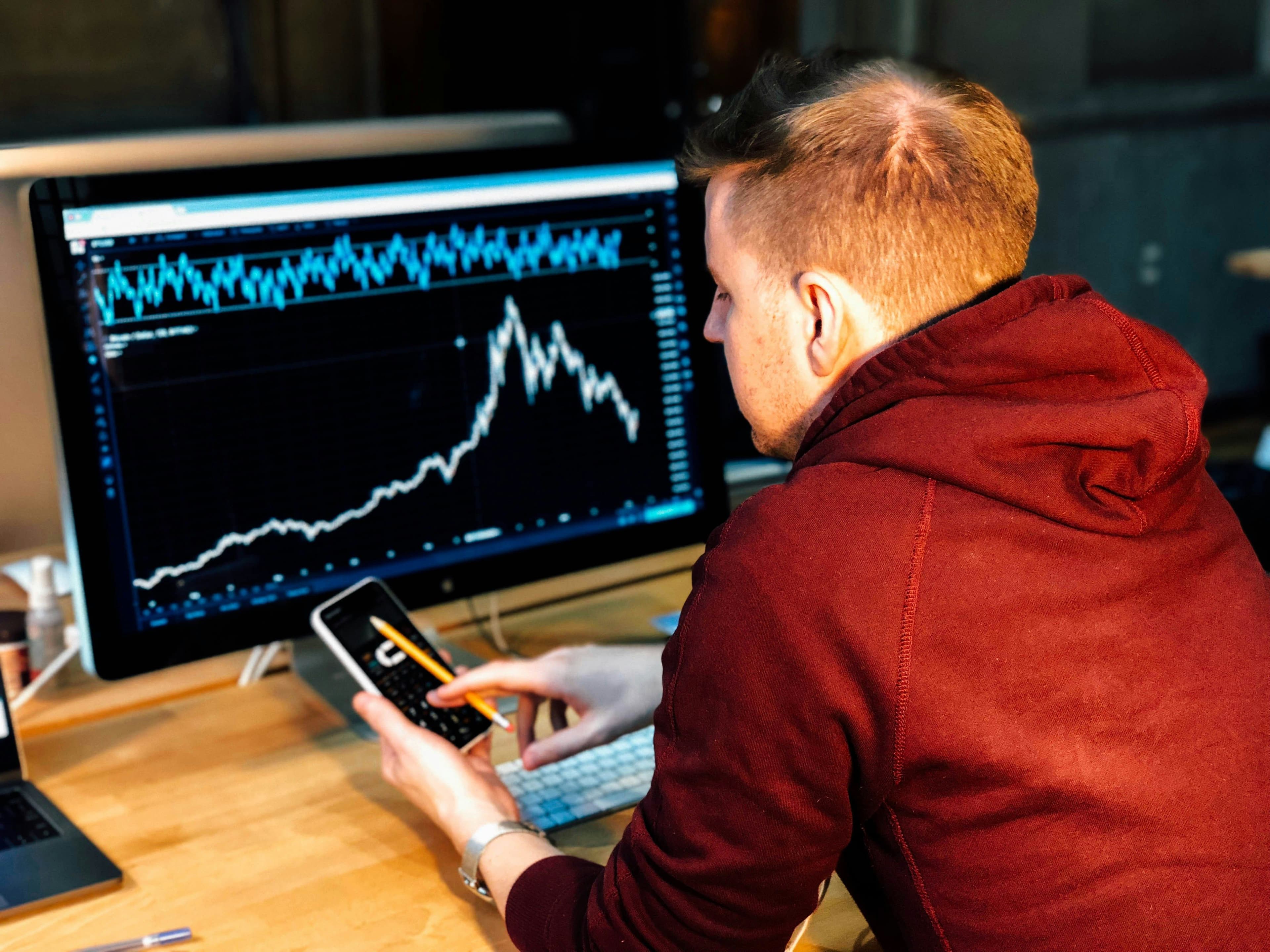 A trader checks his phone while sitting in front of a screen with charts. (Pixabay)